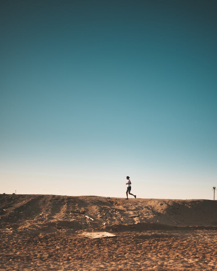 gallery-02 A person jogs on a sandy path with a vast blue sky above, capturing movement and freedom.