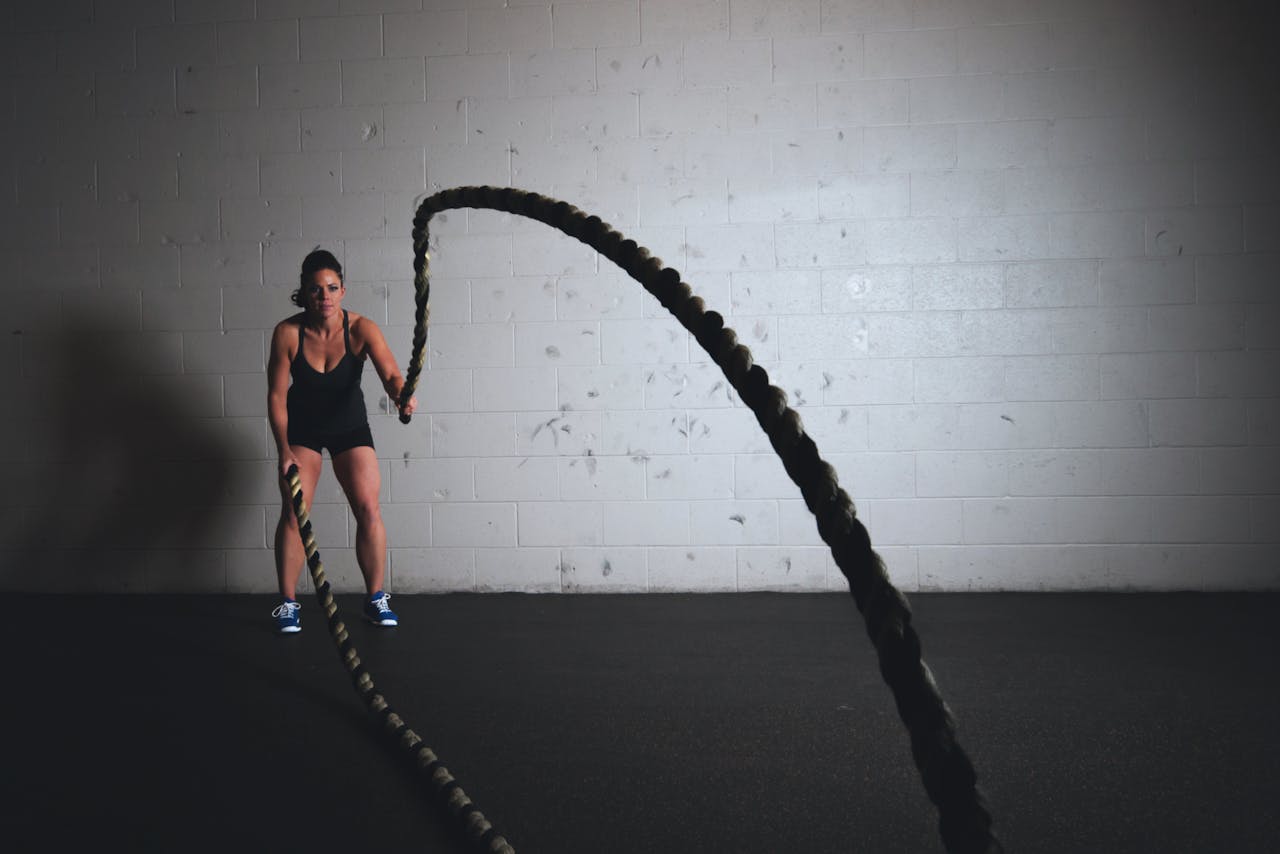 about-img-01 A focused woman performs a dynamic battle rope exercise in a gym setting, demonstrating strength and fitness.